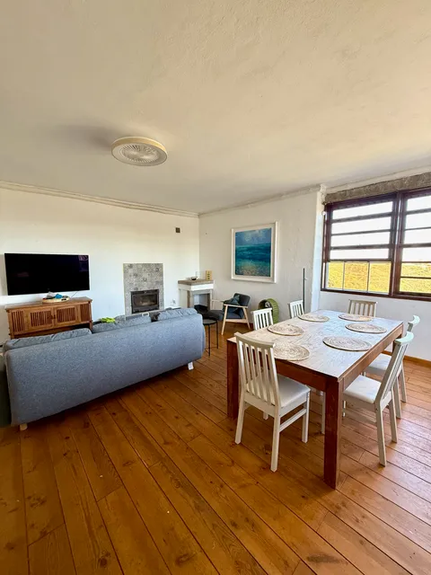 Living room and dining table, with the fireplace and hillside view beyond